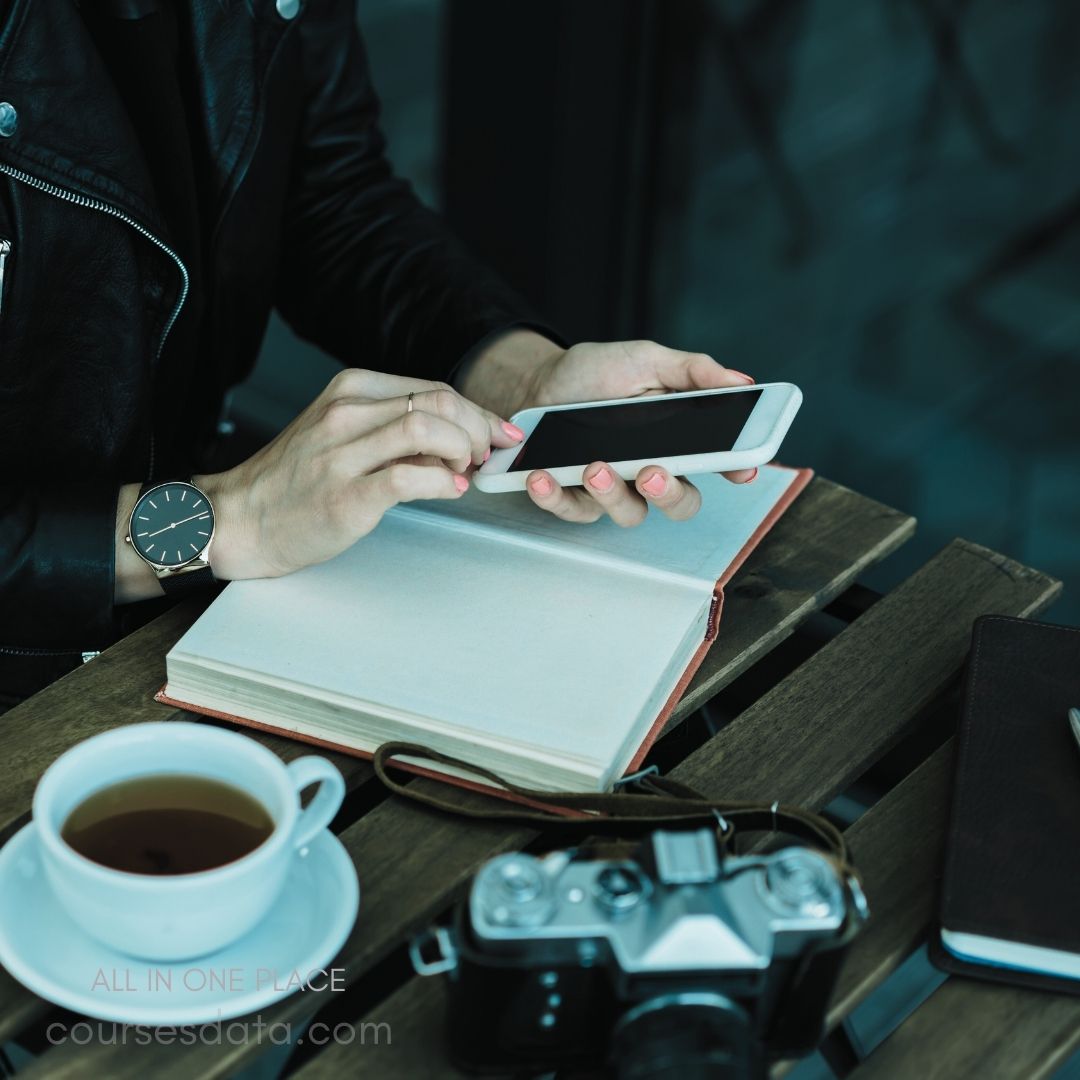 Person using smartphone, notebook, coffee, vintage camera.