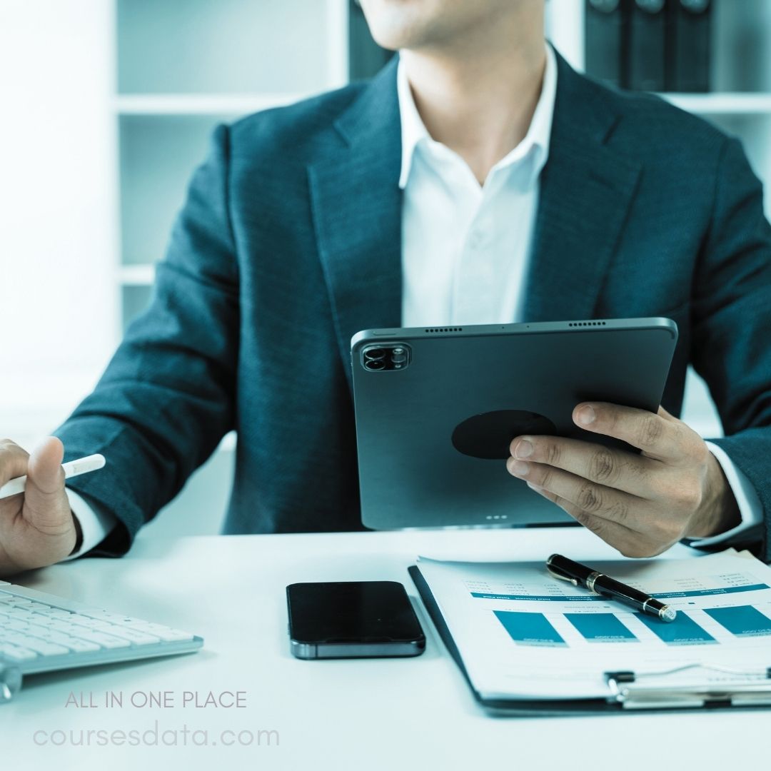 Business professional using tablet. White shirt, dark blazer. Smartphone beside paperwork. Graph charts on clipboard. Stylus in left hand.