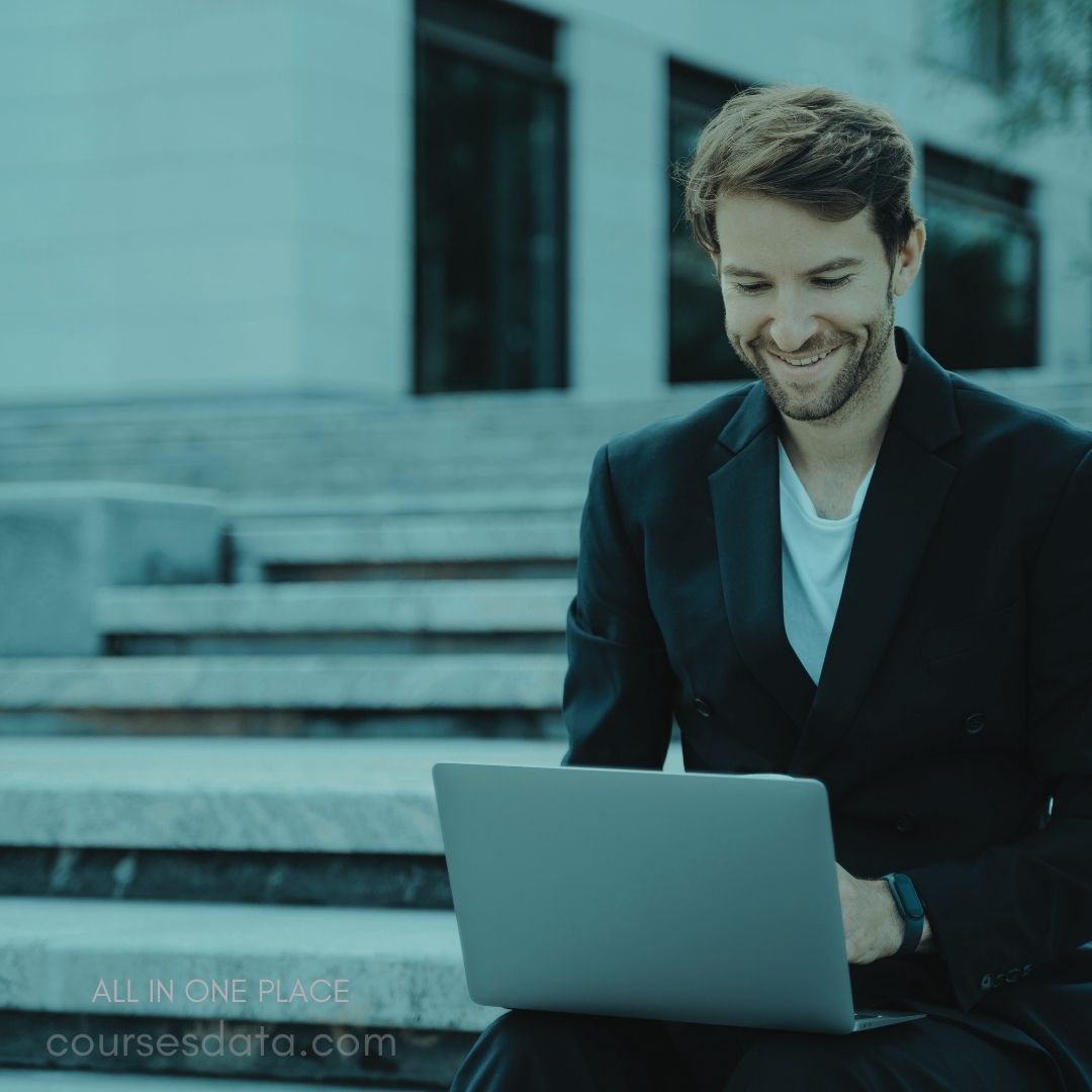 Man in suit smiling, laptop, outdoor steps.
