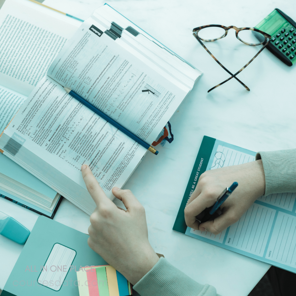 Open textbook, study notes. Hand pointing, pencil on pages. Writing with blue pen, planner. Glasses and calculator nearby.