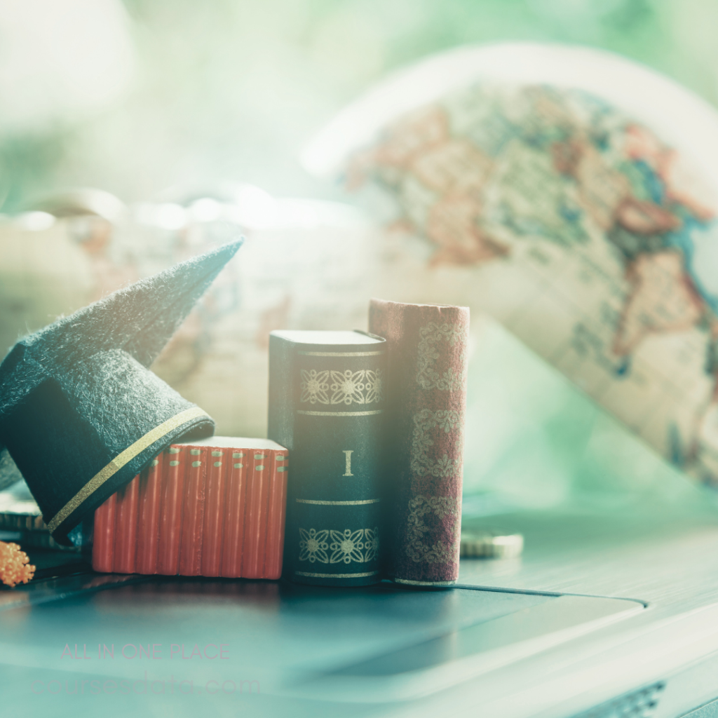 Graduation cap on books. Stacked vintage books displayed. Blurred globe background. Warm, soft lighting effect. Laptop partially visible underneath.