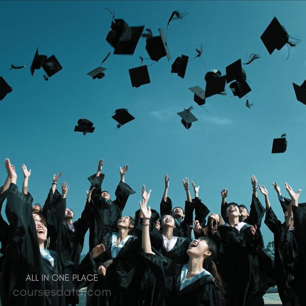 Graduates celebrating together joyfully. Black gowns and caps thrown. Bright blue sky backdrop. Expressions of happiness and excitement.