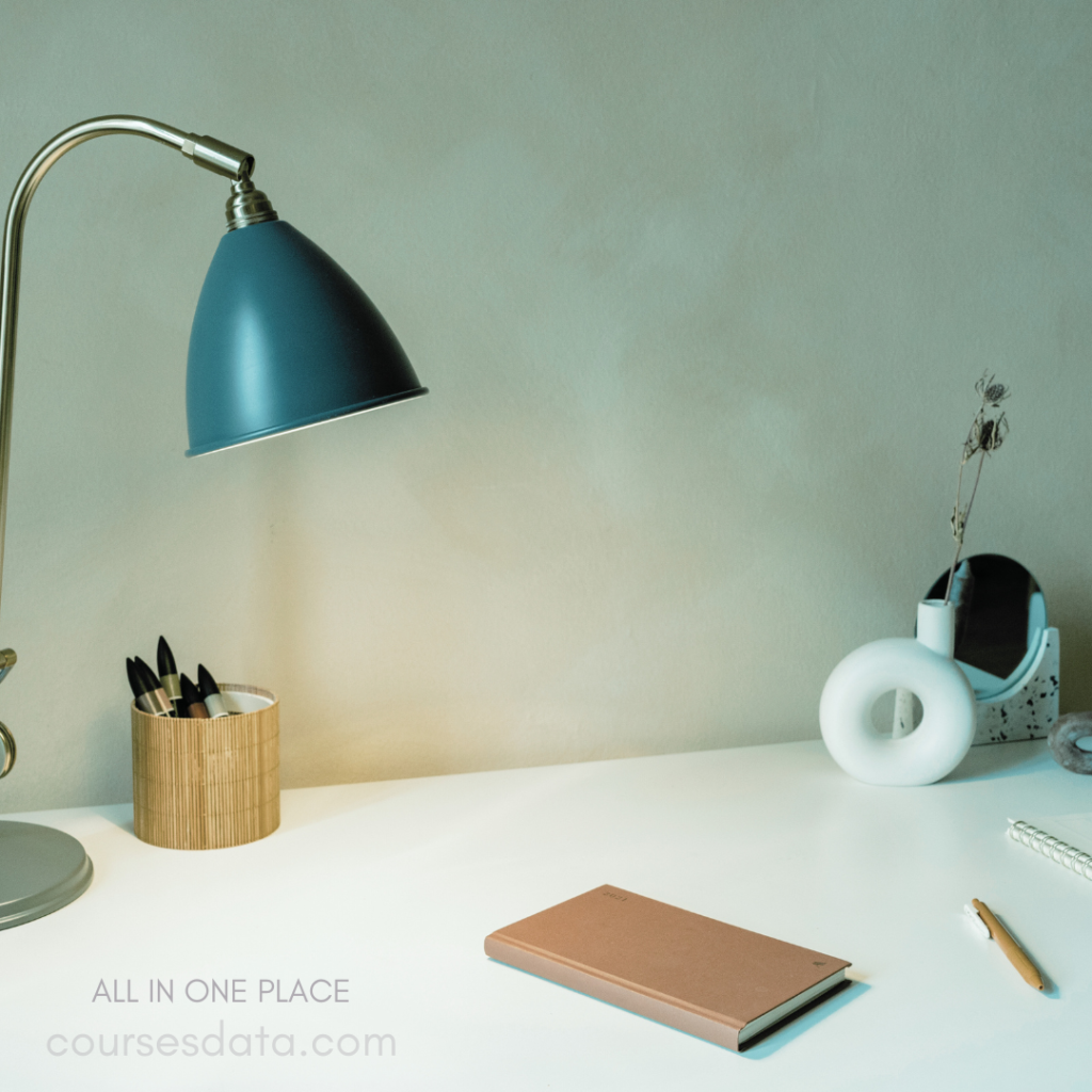 Desk with green lamp. Notebooks and pens. Decorative items displayed. Calming, minimalistic workspace. Warm, inviting atmosphere.