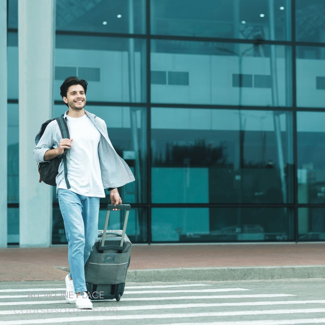 Smiling man with suitcase, backpack. Urban airport setting, striped crosswalk. Casual attire, sunny day.