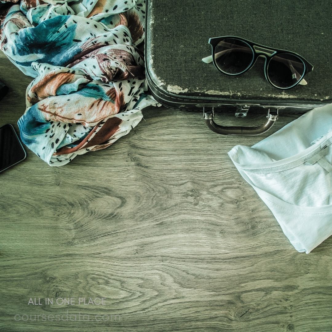 Colorful scarf, vintage suitcase, sunglasses, white shirt, wooden surface.
