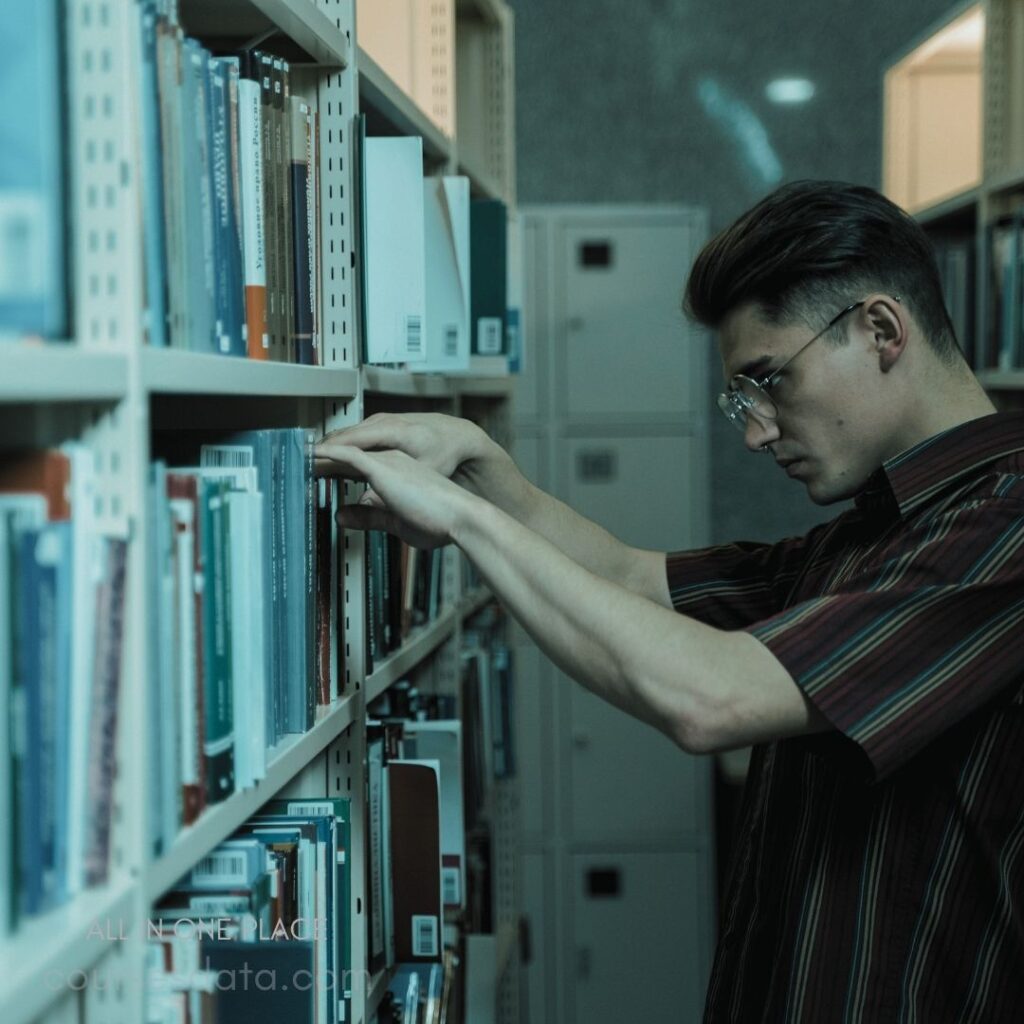 Person organizing library books. Striped shirt, glasses worn. Focused expression, deep concentration. Bookshelves lined with books. Background features lockers.