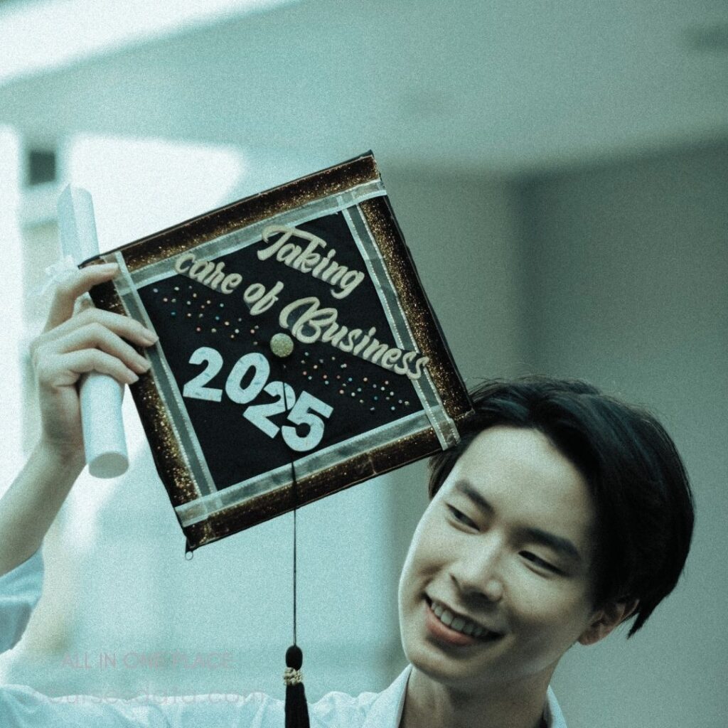 Graduation cap with text. "Taking care of Business 2025." Smiling young man holding diploma. Blurred background with soft lighting.