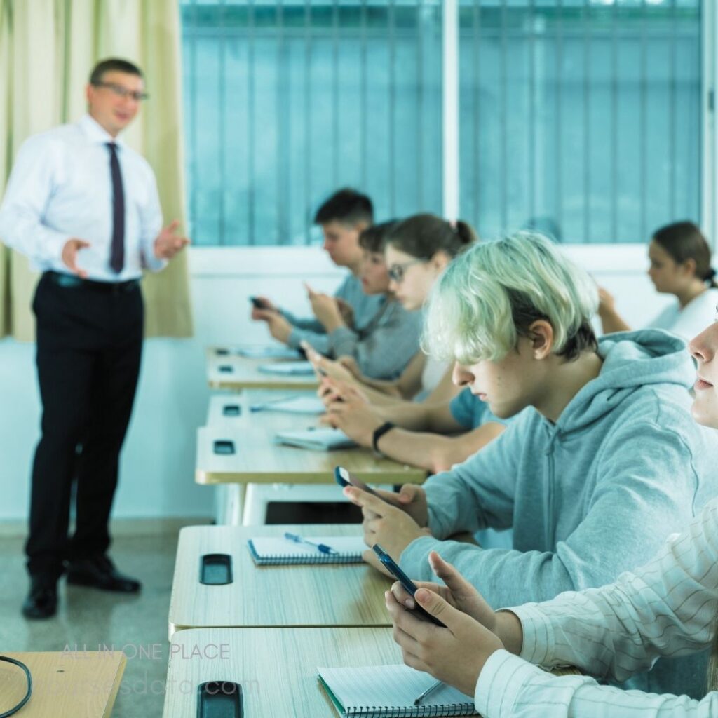 Teacher speaking to students. Students using smartphones. Classroom with notebooks visible. Bright, modern learning environment. Focused student engagement.