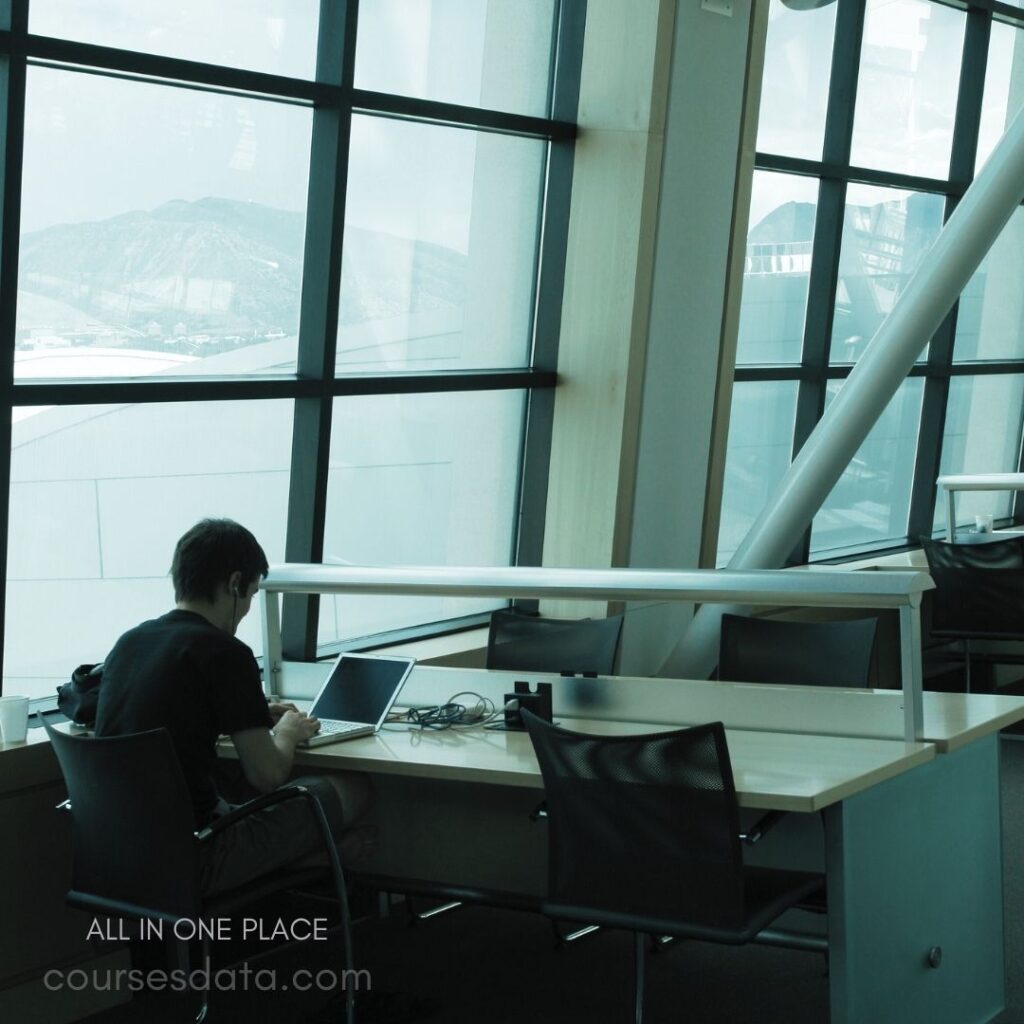 Person working on laptop. Bright, large window view. Minimalist workspace design. Mountains visible in background. Quiet, focused atmosphere.