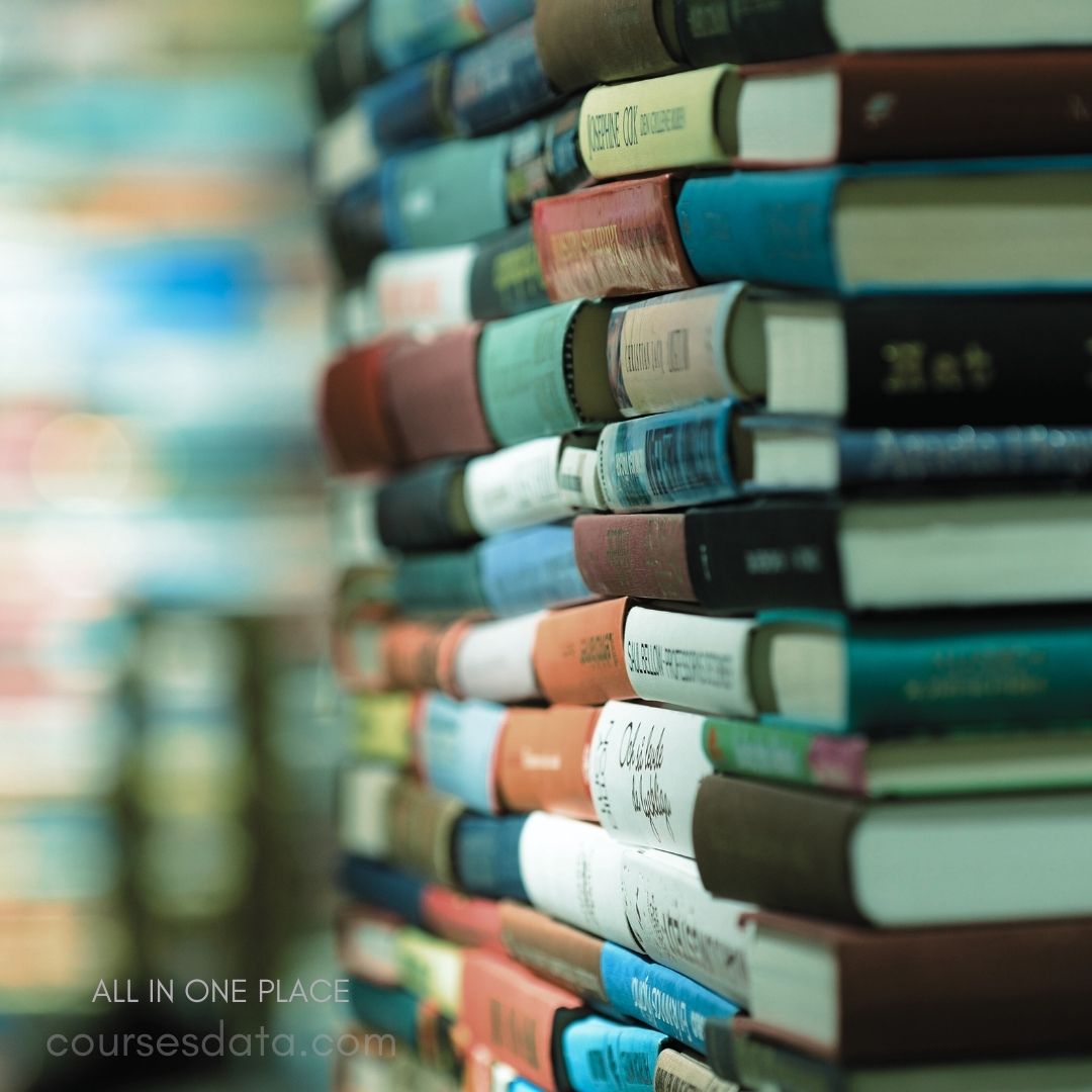 Stacked books in various colors. Blurred background with more books. Close-up of book spines visible. Diverse titles and sizes showcased.