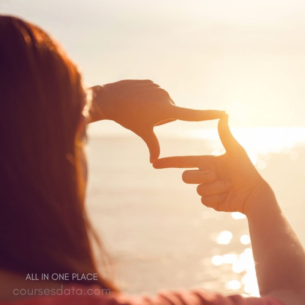 Person framing sunset view. Golden sunlight reflecting water. Hands creating a rectangular shape. Soft focus on surrounding area.