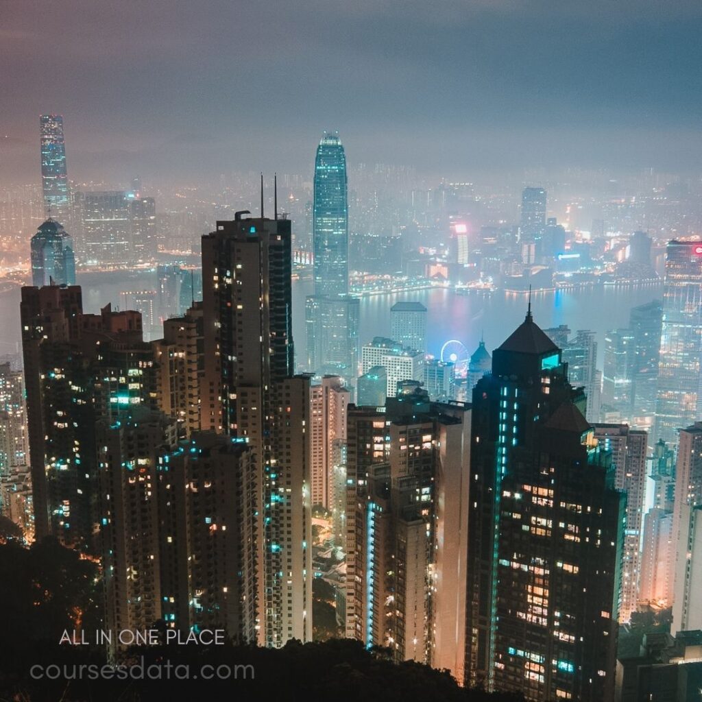 City skyline at night. Tall skyscrapers illuminated. Foggy atmosphere with lights. Harbor view in background. Colorful city lights shining.