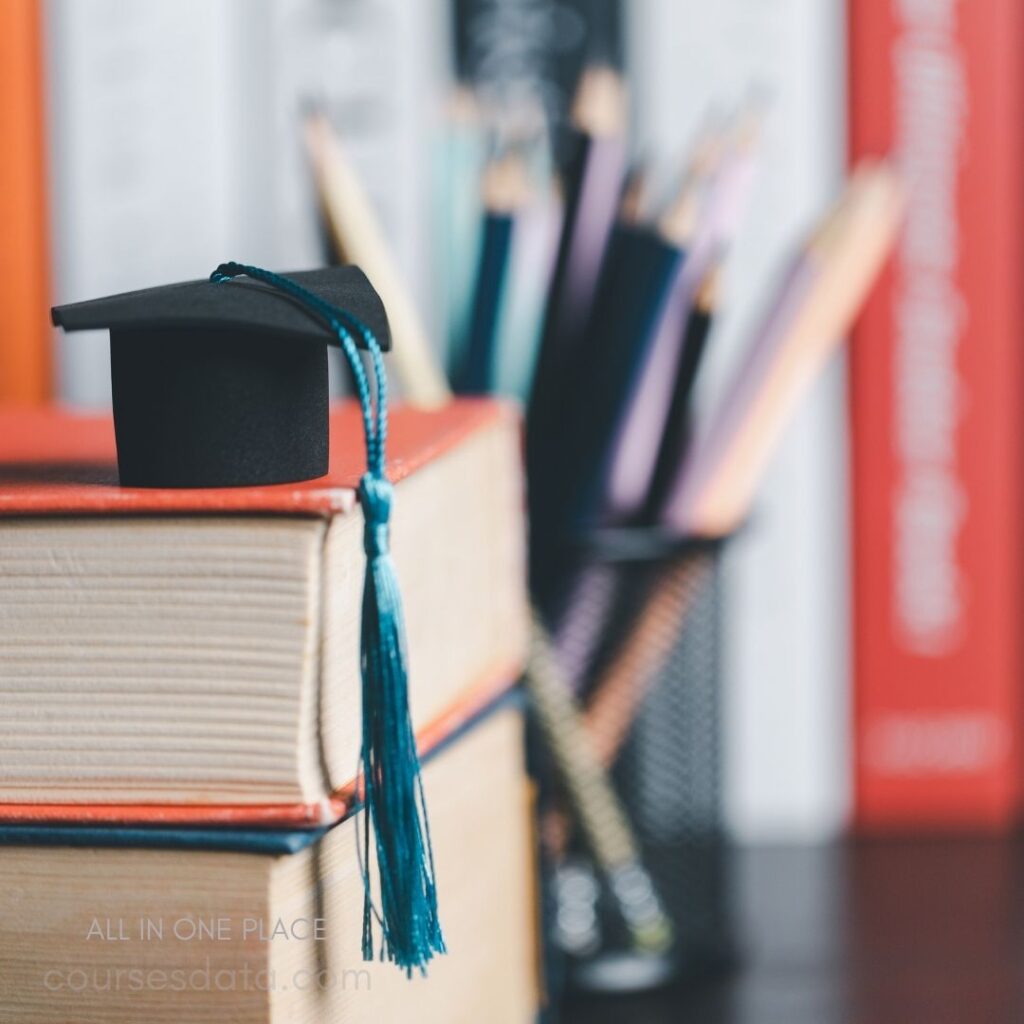 Graduation cap on books. Colorful pencils in holder. Blurred background with books.