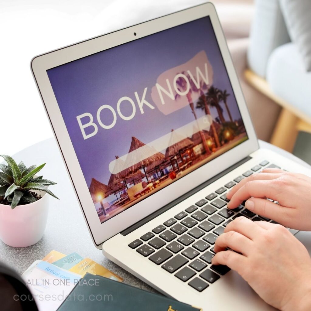 Laptop displaying travel booking site. Hand typing on keyboard. Succulent plant beside laptop. Credit cards on table. Tropical vacation image background.