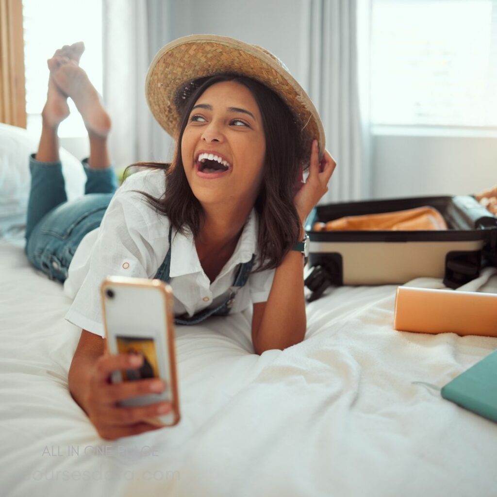 Laughing young woman, straw hat. Relaxing on bed, holding phone. Luggage beside her, casual outfit. Bright room, natural light streaming. Joyful expression, carefree mood.