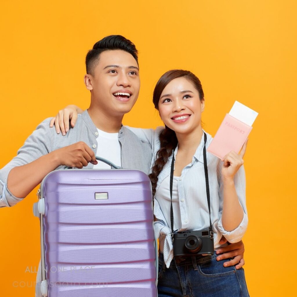 Couple with luggage and camera. Bright orange background. Smiling, excited expressions. Woman holding passport. Purple suitcase in foreground.