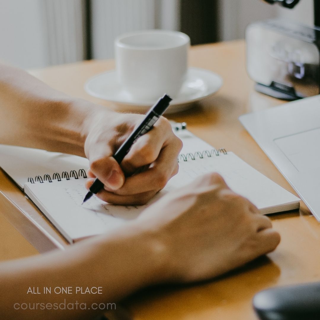 Writing in a notebook, coffee cup.