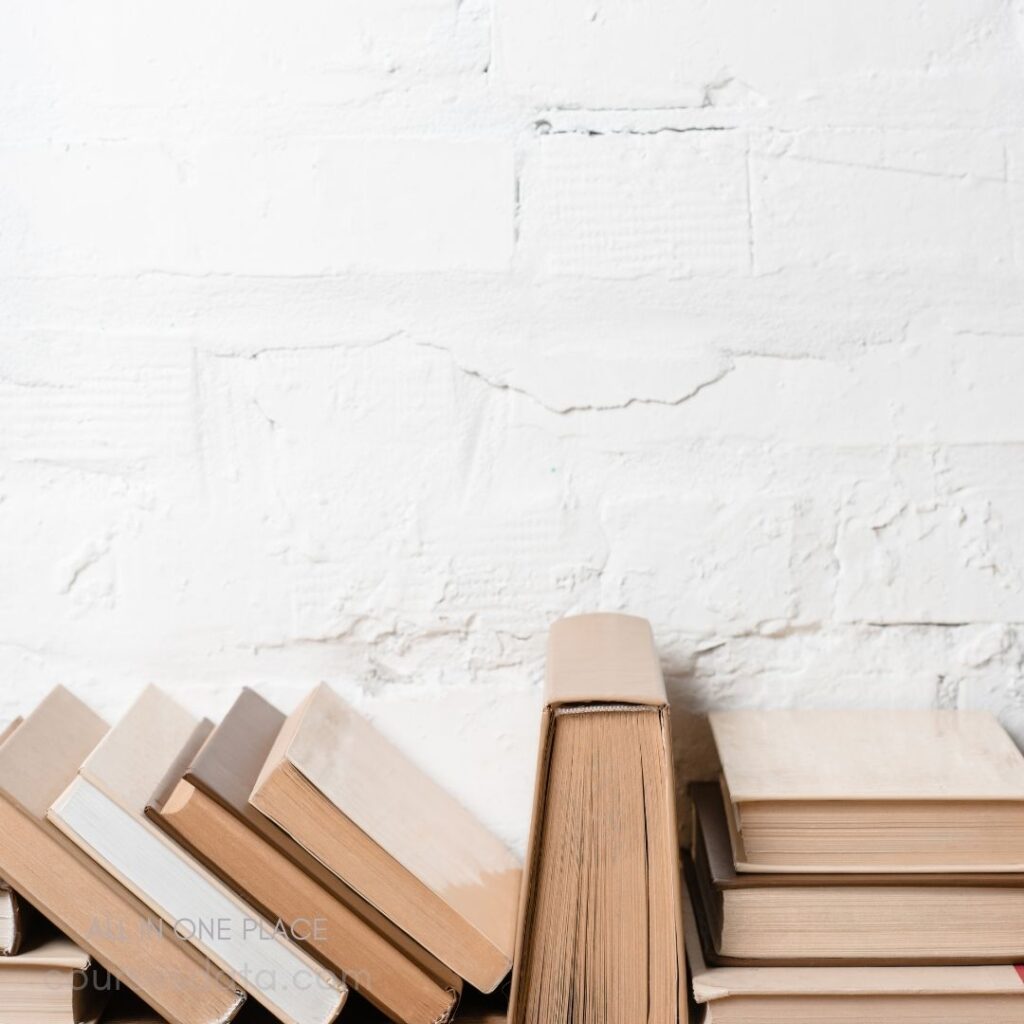 Stacked books against a white wall.