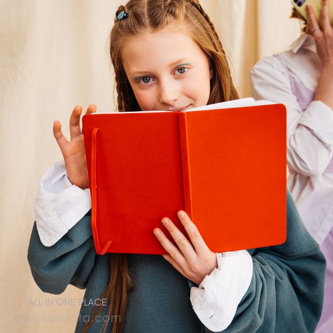 Girl holding red notebook smiling.