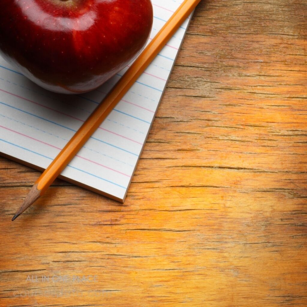 Apple, pencil, notepad on wood.