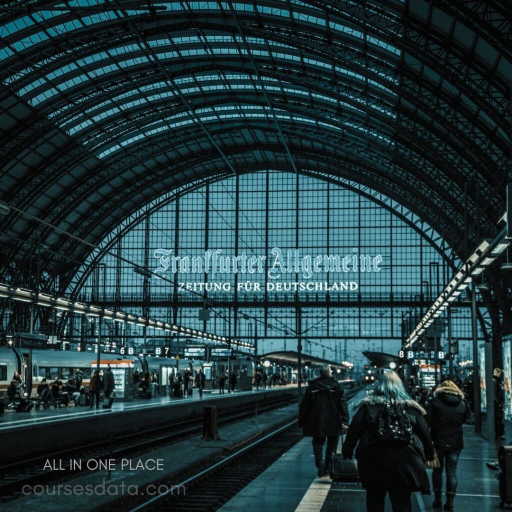 Train station at dusk. Frankfurter Allgemeine headline visible. People walking along platform. Modern glass architecture. Trains and signage in background.