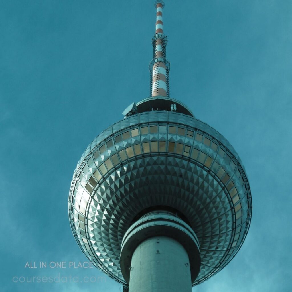 TV tower against blue sky. Geometric dome structure. Red and white antenna. Observation deck visible. Urban architectural landmark.