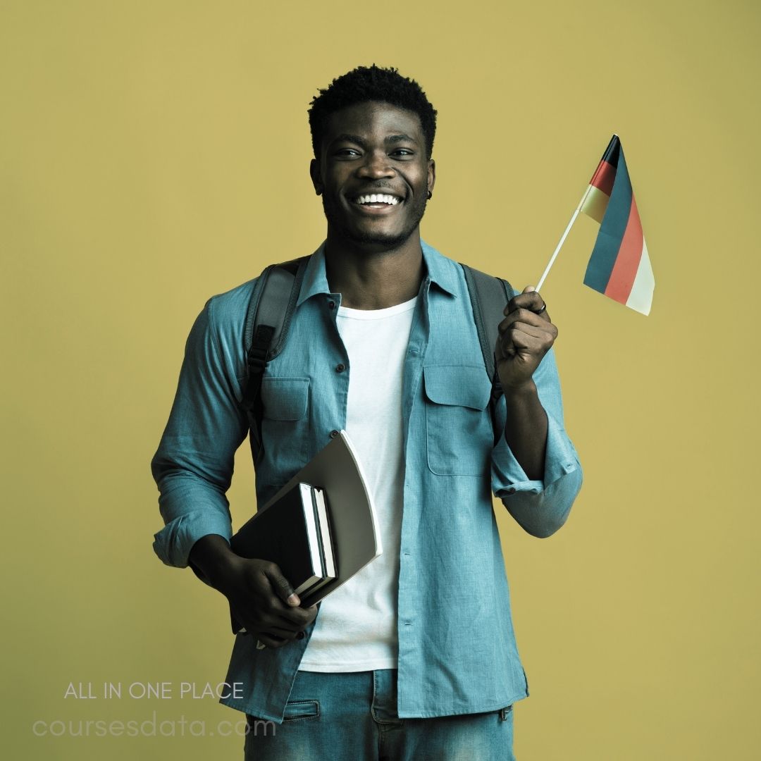 Smiling man holding German flag. Wearing blue shirt and backpack. Books held in left arm. Bright yellow background. Cheerful, confident expression.