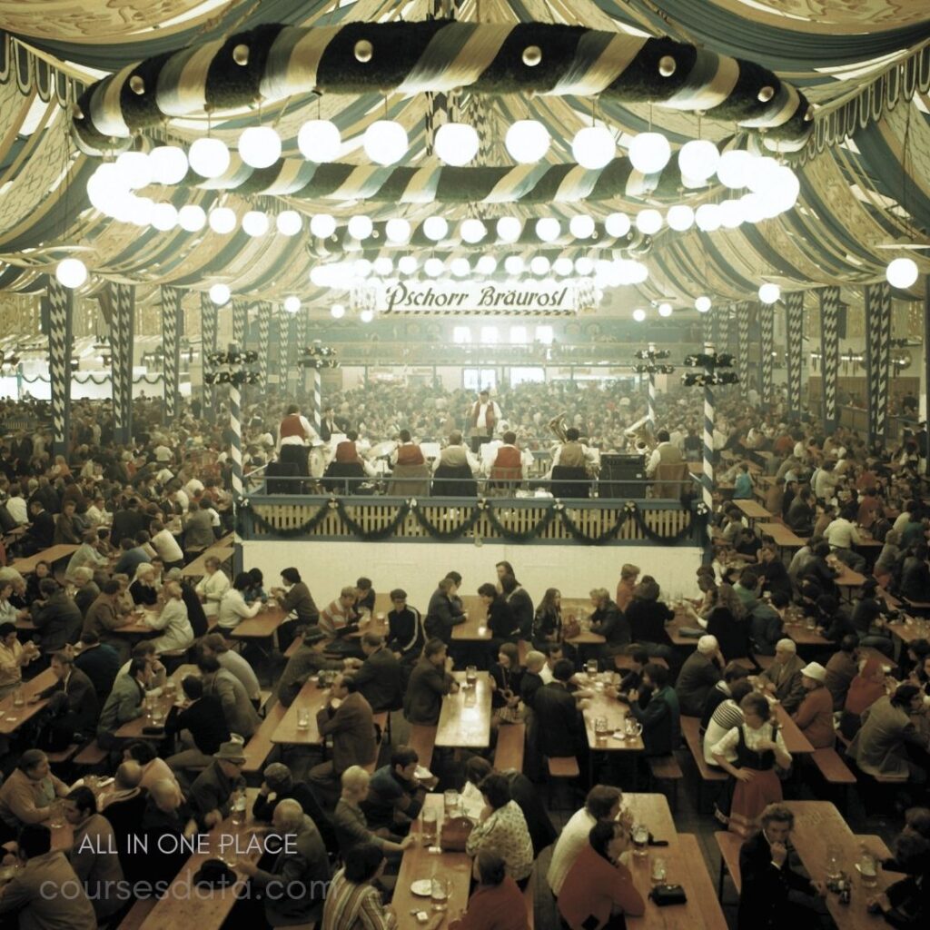 Crowded beer hall atmosphere. Colorful striped ceiling decor. Long wooden tables filled. Live band performing on stage. People enjoying food and drinks.