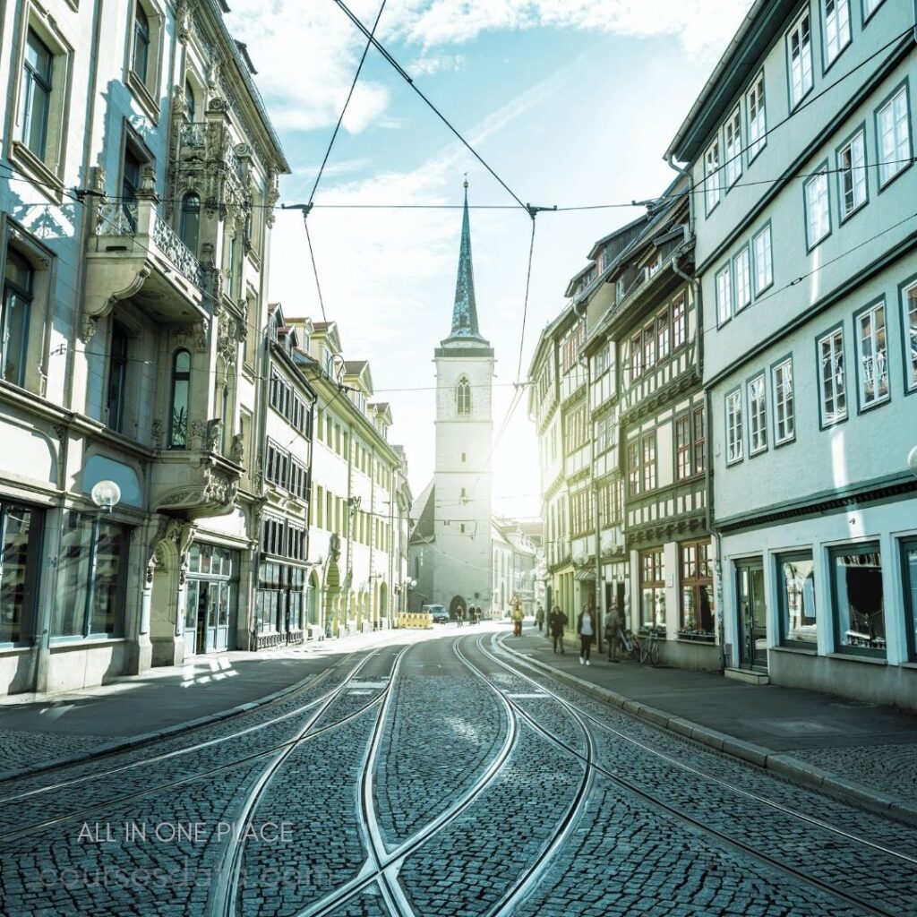 Historic street with church. Cobblestone pavement and tramlines. Sunlight illuminating buildings. People walking along the street. Traditional architecture lining pathway.