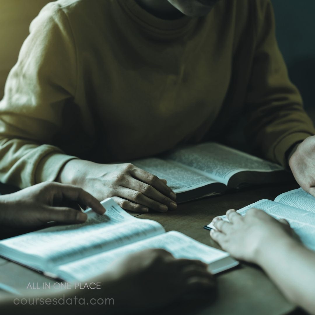 Group studying open books. Hands examining text closely. Warm lighting sets atmosphere. Wooden table surfaces visible. Focused collaborative learning moment.