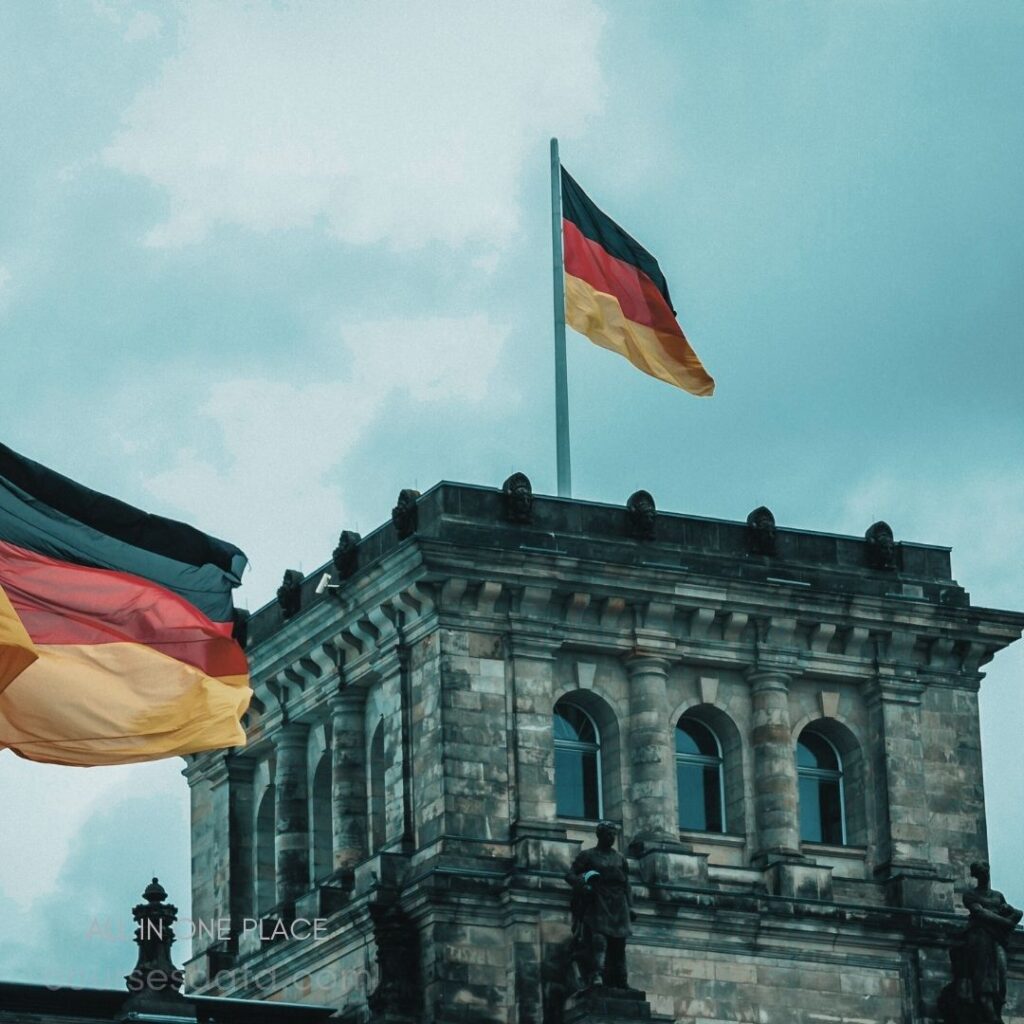 German flags flying high. Historic stone building backdrop. Overcast sky, dramatic atmosphere. Architectural details are prominent. Symbol of national pride.