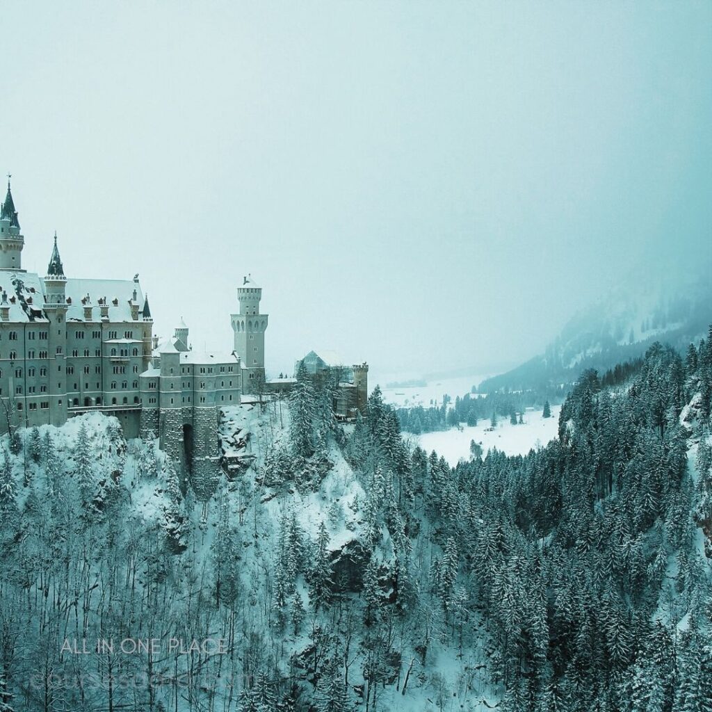 Snowy castle on hillside. Surrounded by dense forest. Foggy winter landscape backdrop. Majestic towers and spires. Peaceful, serene atmosphere.