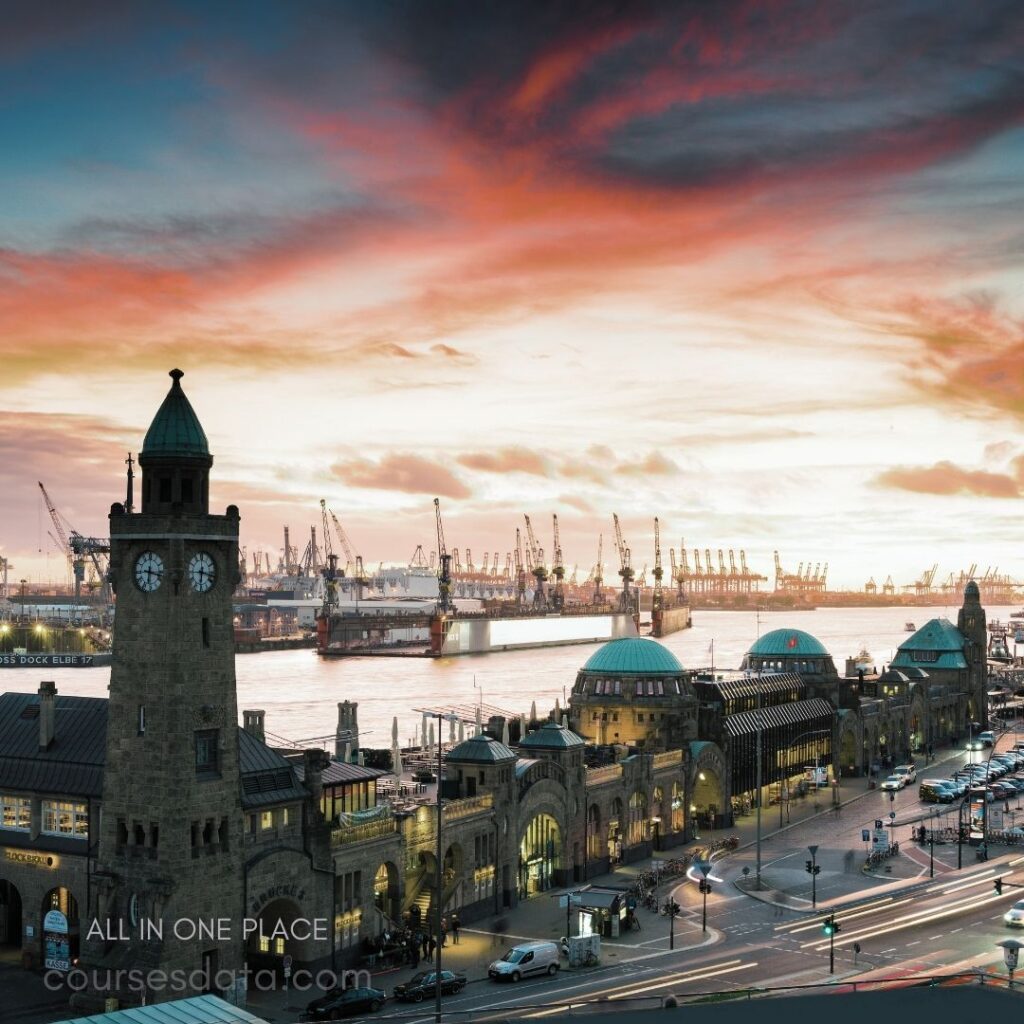 Historic harbor clock tower. Vibrant sunset sky. Bustling port activities visible. Scenic waterfront architecture. Illuminated streets below.