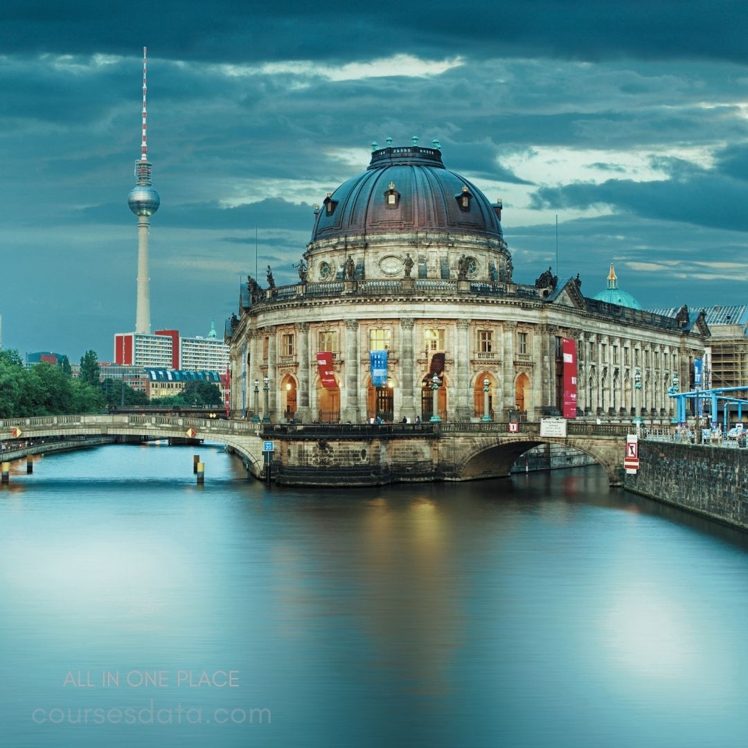 Historic museum building, Berlin. TV tower in background. Calm water reflection. Dramatic cloudy sky. Bridges crossing the river.