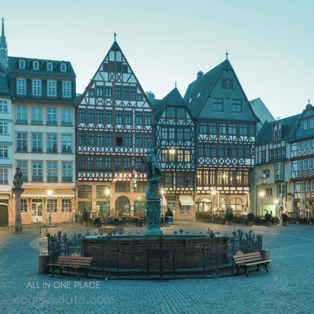 Historic square with fountain. Traditional half-timbered buildings. Evening ambiance with soft lighting. Stone-paved ground with benches. Quiet, charming urban setting.