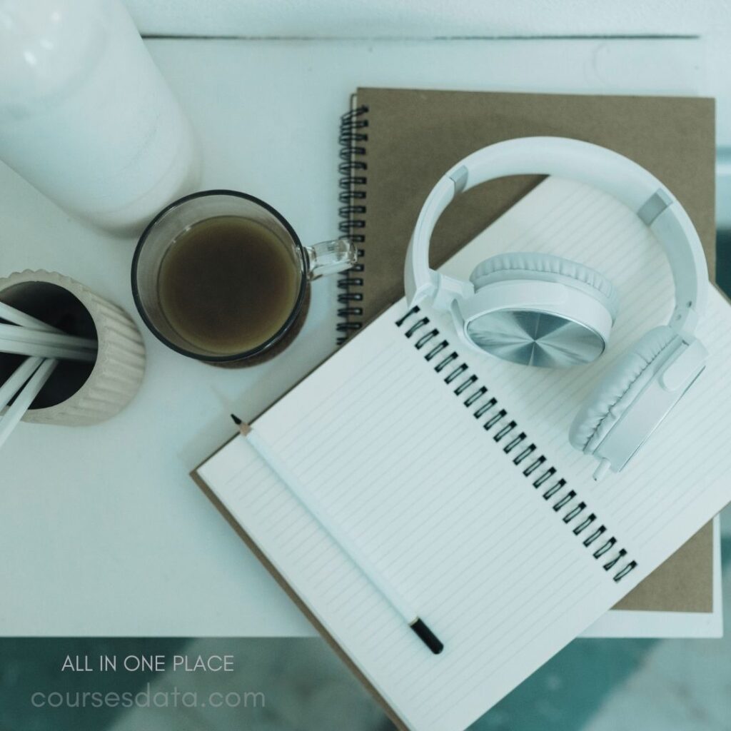 Notebook, white headphones, coffee cup.