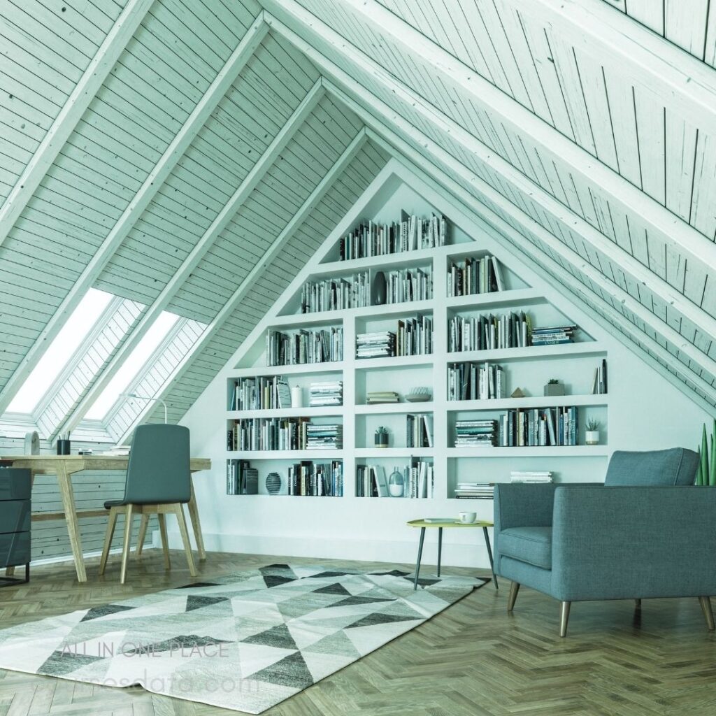 Attic room with slanted ceiling. Large bookshelf filled with books. Wooden desk and grey chair. Geometric patterned rug on floor. Minimalist green accent chair.