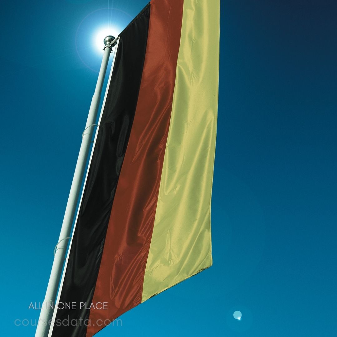 German flag waving brightly. Bold black, red, yellow stripes. Clear blue sky backdrop. Sunlight illuminating the flag.
