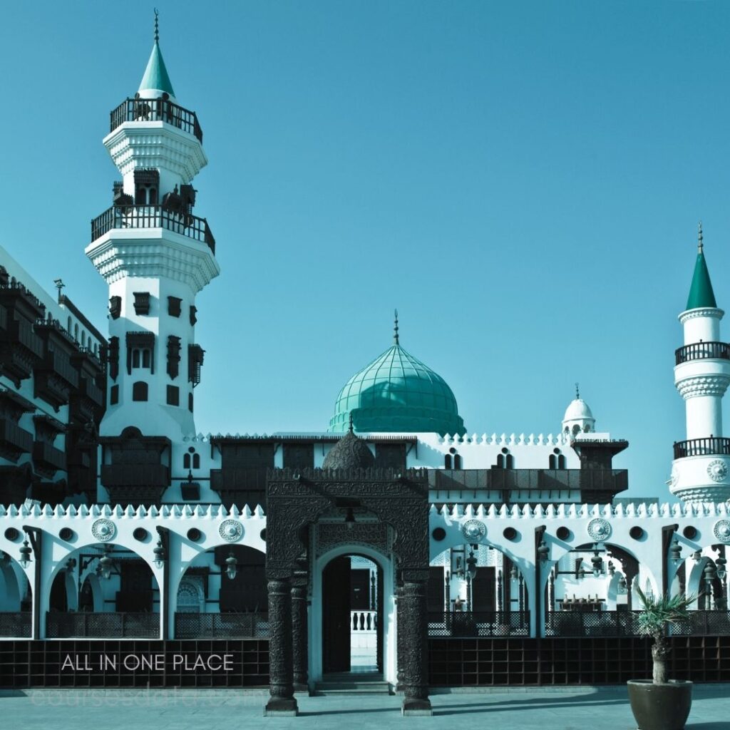 Historic building with towers. Green dome and minaret. Intricate architectural details. Clear blue sky backdrop. Welcoming entrance archway.