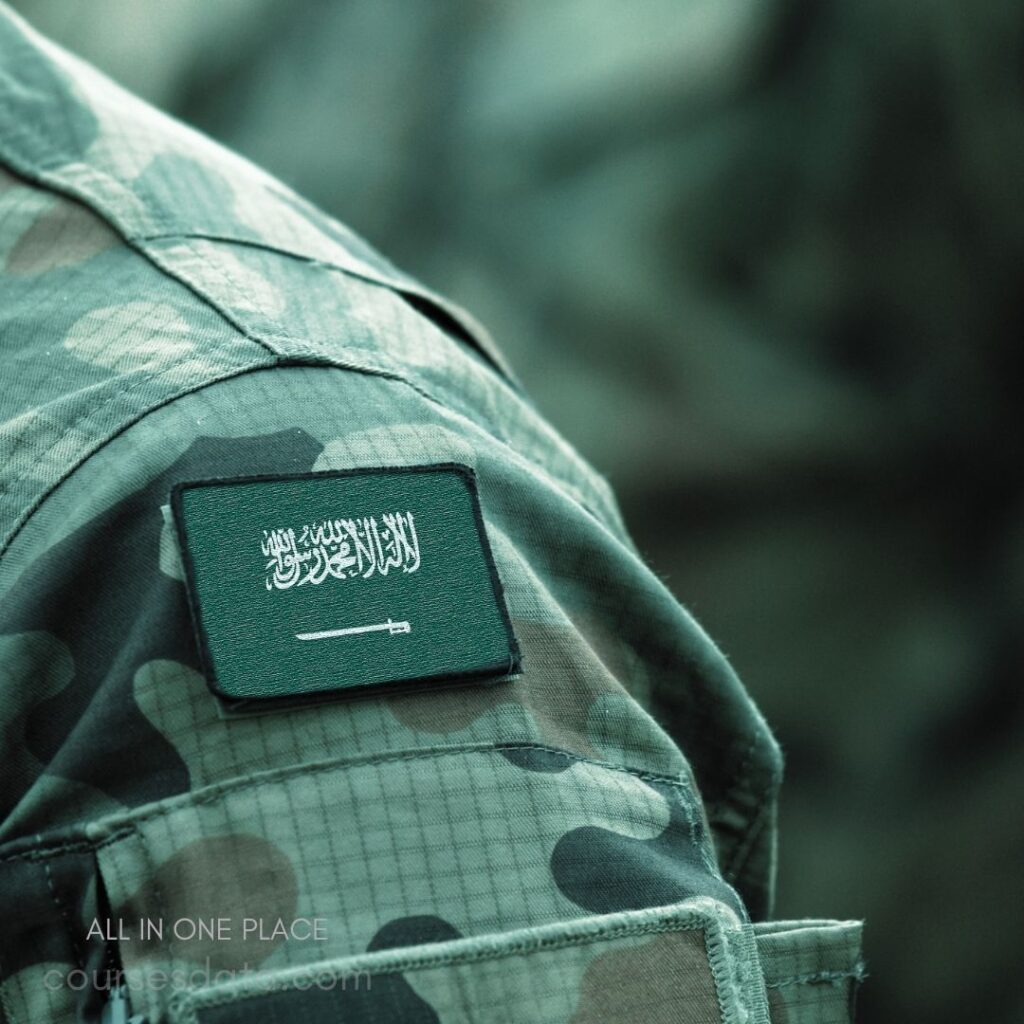 Military uniform shoulder patch. Green background with Arabic script. Sword emblem displayed prominently. Camouflage fabric texture visible. Close-up perspective of emblem.