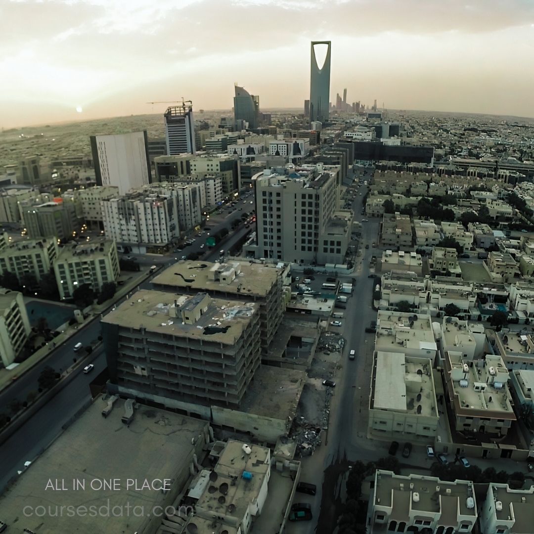 Aerial view of Riyadh city. Modern skyscrapers against sunset. City streets bustling with cars. Diverse architecture and urban landscape. Golden hues illuminate the horizon.