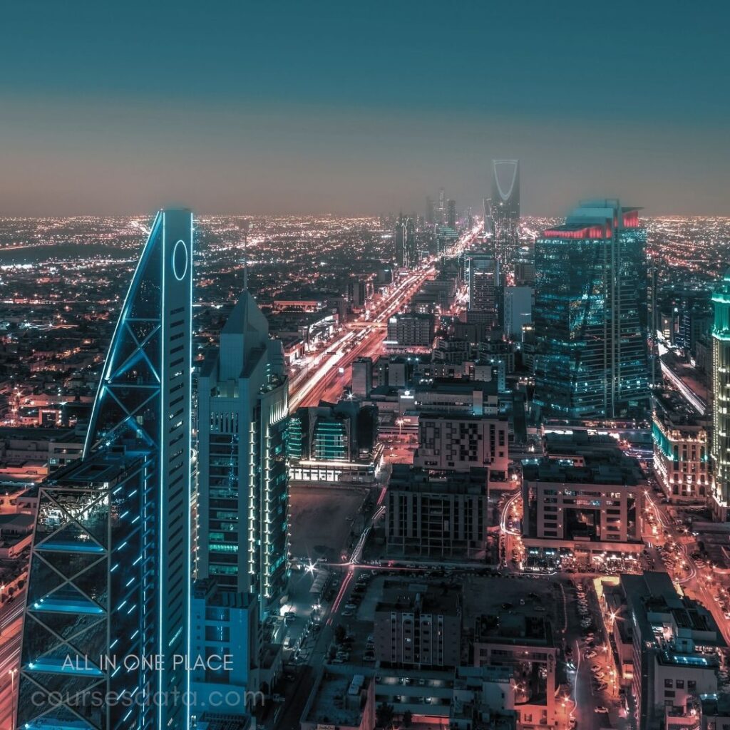 Night cityscape of Riyadh. Illuminated skyscrapers at dusk. Main road bustling with traffic. Vibrant lights and urban skyline. Prominent triangular tower featured.