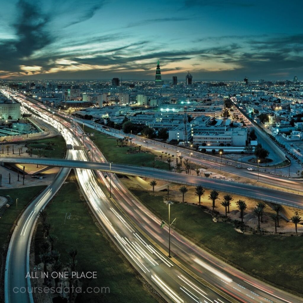 City skyline at dusk. Illuminated highway with traffic. Tower in the distance. Palm trees along the road. Colorful sky with clouds.