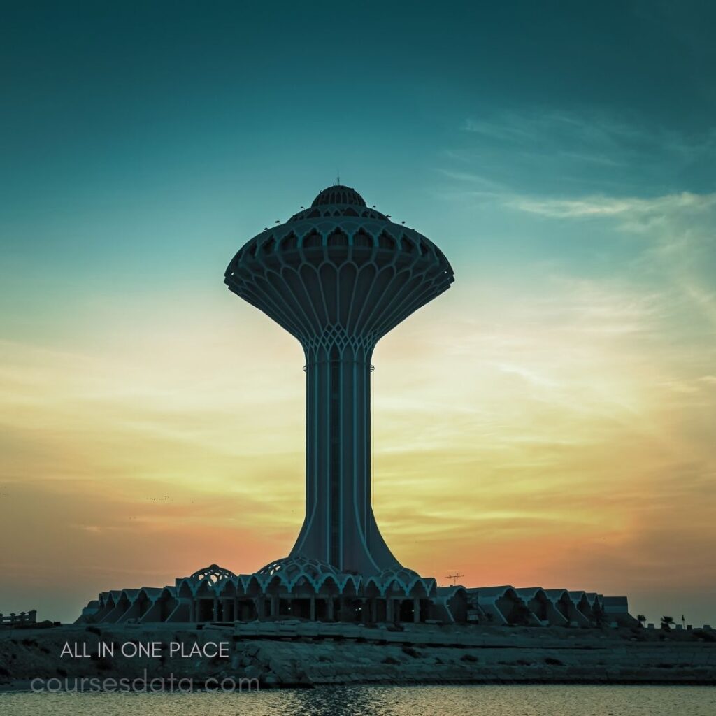 Towering structure against sunset. Unique, modern architectural design. Reflective water in foreground. Soft, colorful sky backdrop.