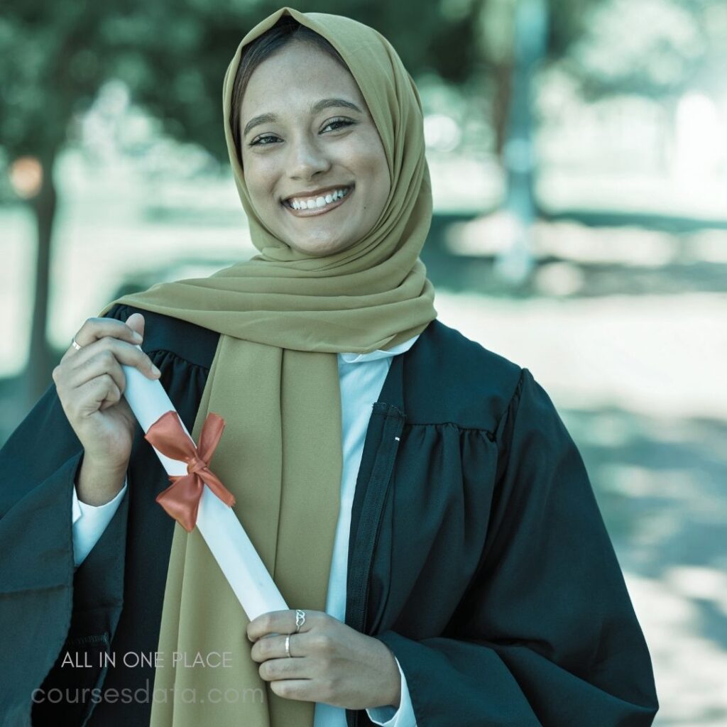 Graduating woman in hijab. Smiling, holding diploma scroll. Greenery background, joyful moment. Black graduation gown, white shirt. Ribbon tied on diploma.