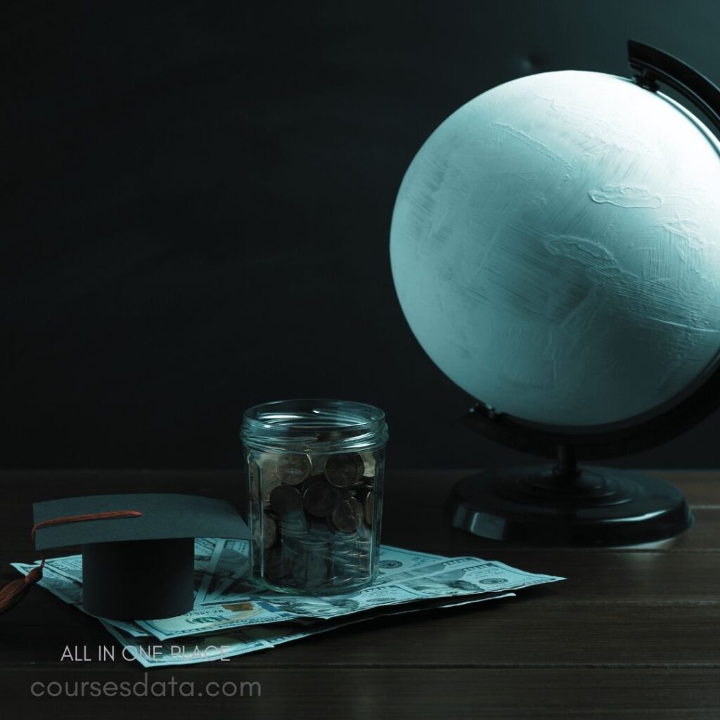 Globe with painted surface, Jar filled with coins, Graduation cap on bills, Wooden table background.