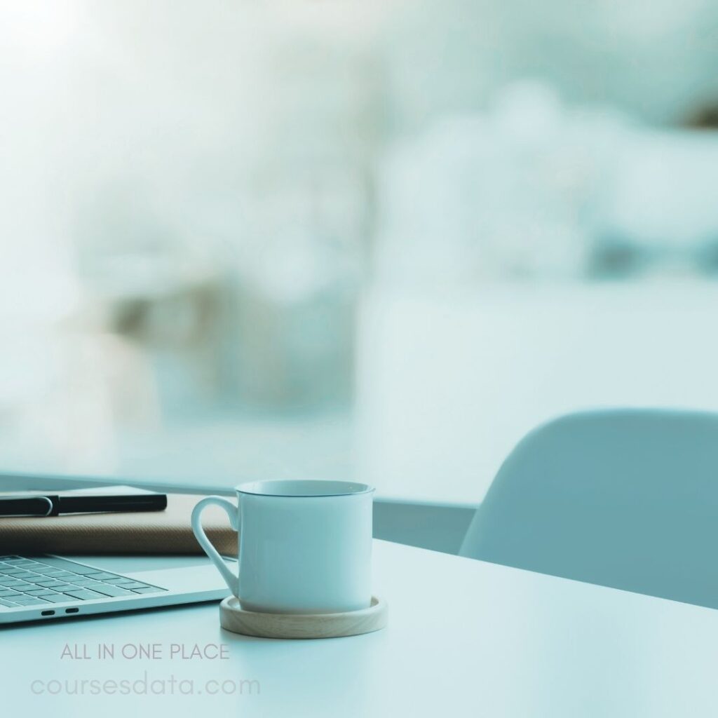 White mug on wooden coasters. Laptop with black stylus. Bright, softly blurred background. Minimalistic workspace aesthetic. Calm, focused environment.