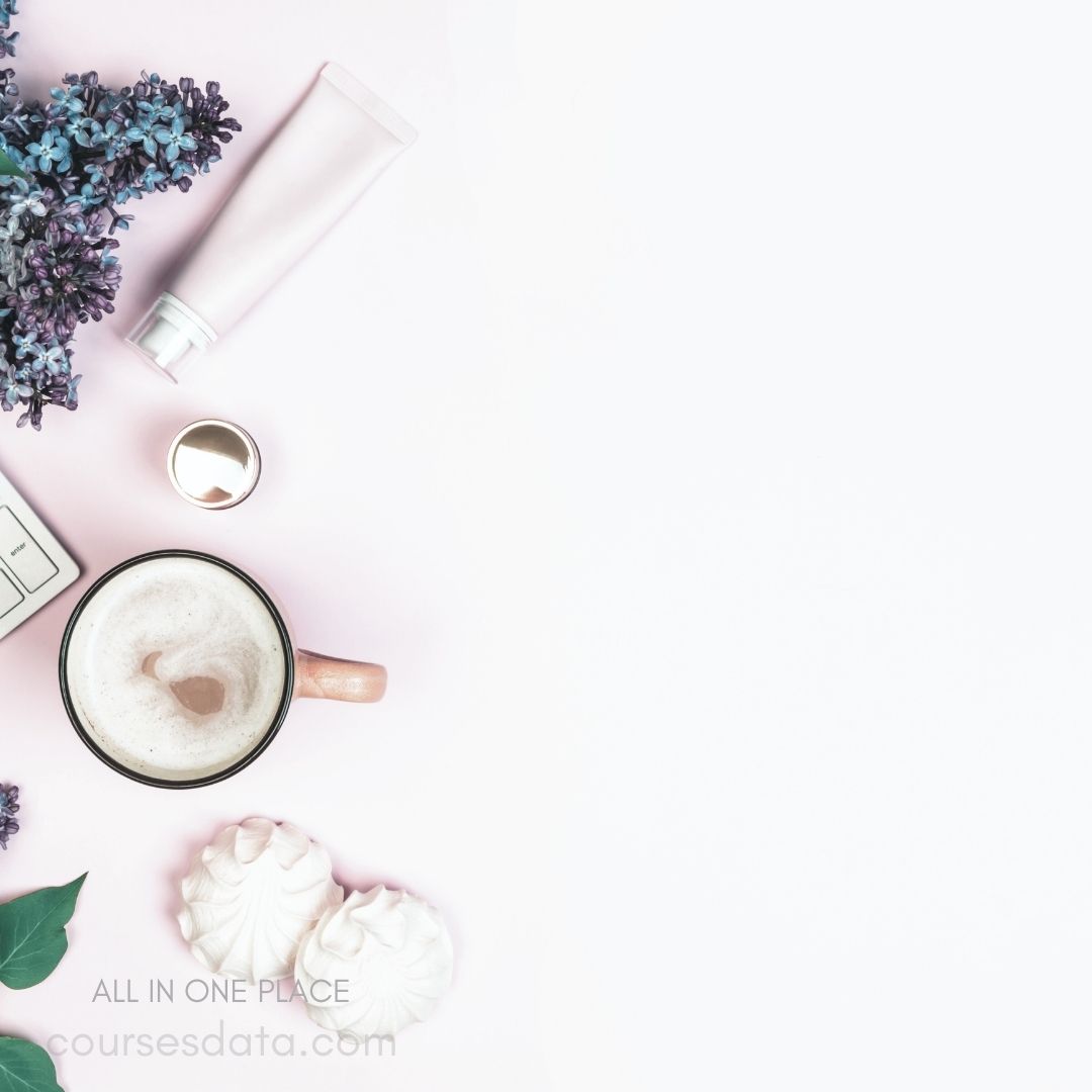 Coffee cup with froth. Purple flowers arranged neatly. White cream tube beside cup. Two shell-shaped meringues present. Minimalist pink background ambiance.