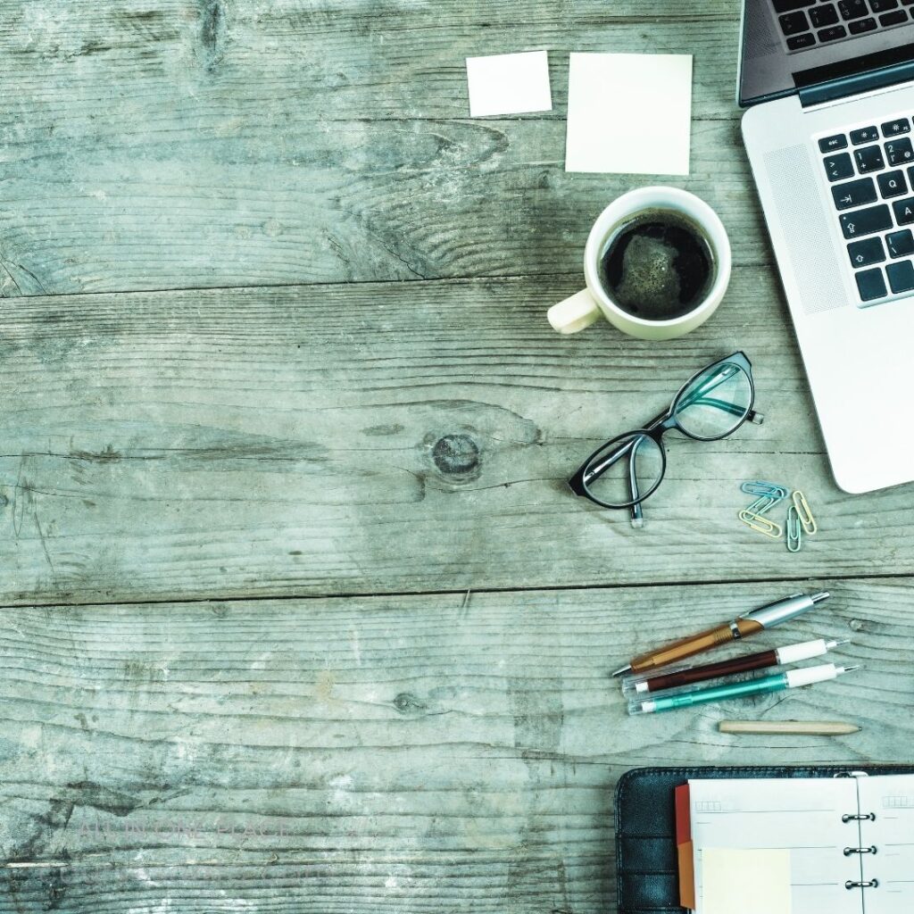 Desk workspace with laptop, coffee. Glasses, stationery, and notes. Wooden surface, organized items. Productive environment for work.