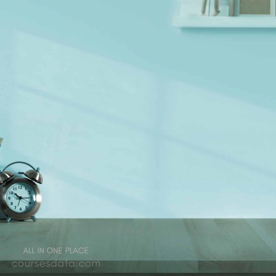 Alarm clock on wooden table. Light blue wall background. Shadows cast on surface. Minimalistic decor style. Website text in foreground.